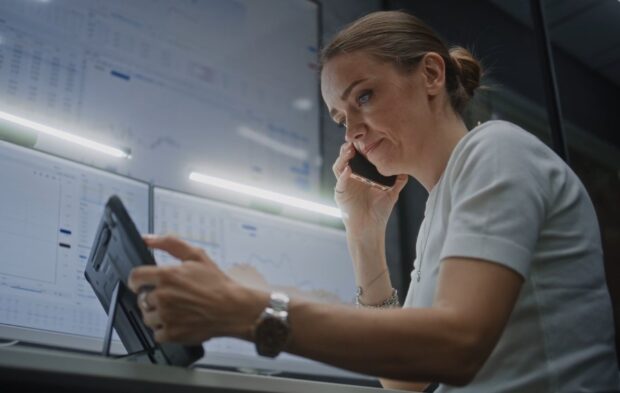 A woman sits at a desk, focused on a tablet computer in front of her