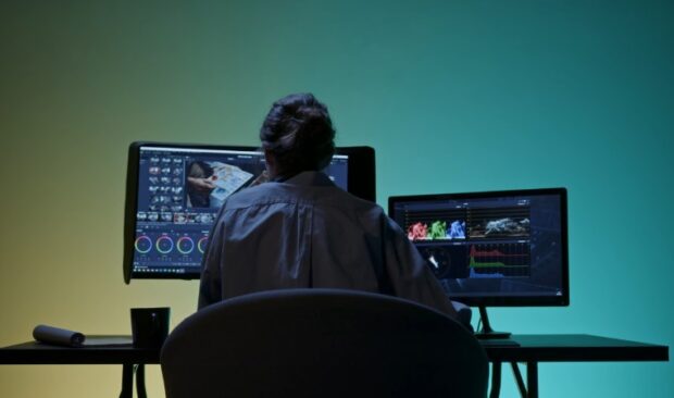 A person sitting at a desk, focused on two computer monitors displaying various applications and documents