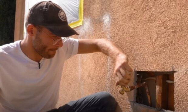 Plumber adjusting an exterior hose bib valve through an access opening in the stucco wall