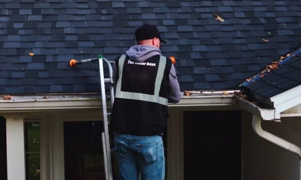 A technician performing routine gutter cleaning services on a residential property