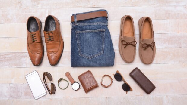 Brown shoes, jeans, belts, watches, wallets, and sunglasses are arranged on a wooden floor