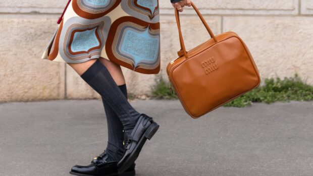 Black loafers, knee socks, patterned skirt, and brown leather bag complete a polished street-style outfit