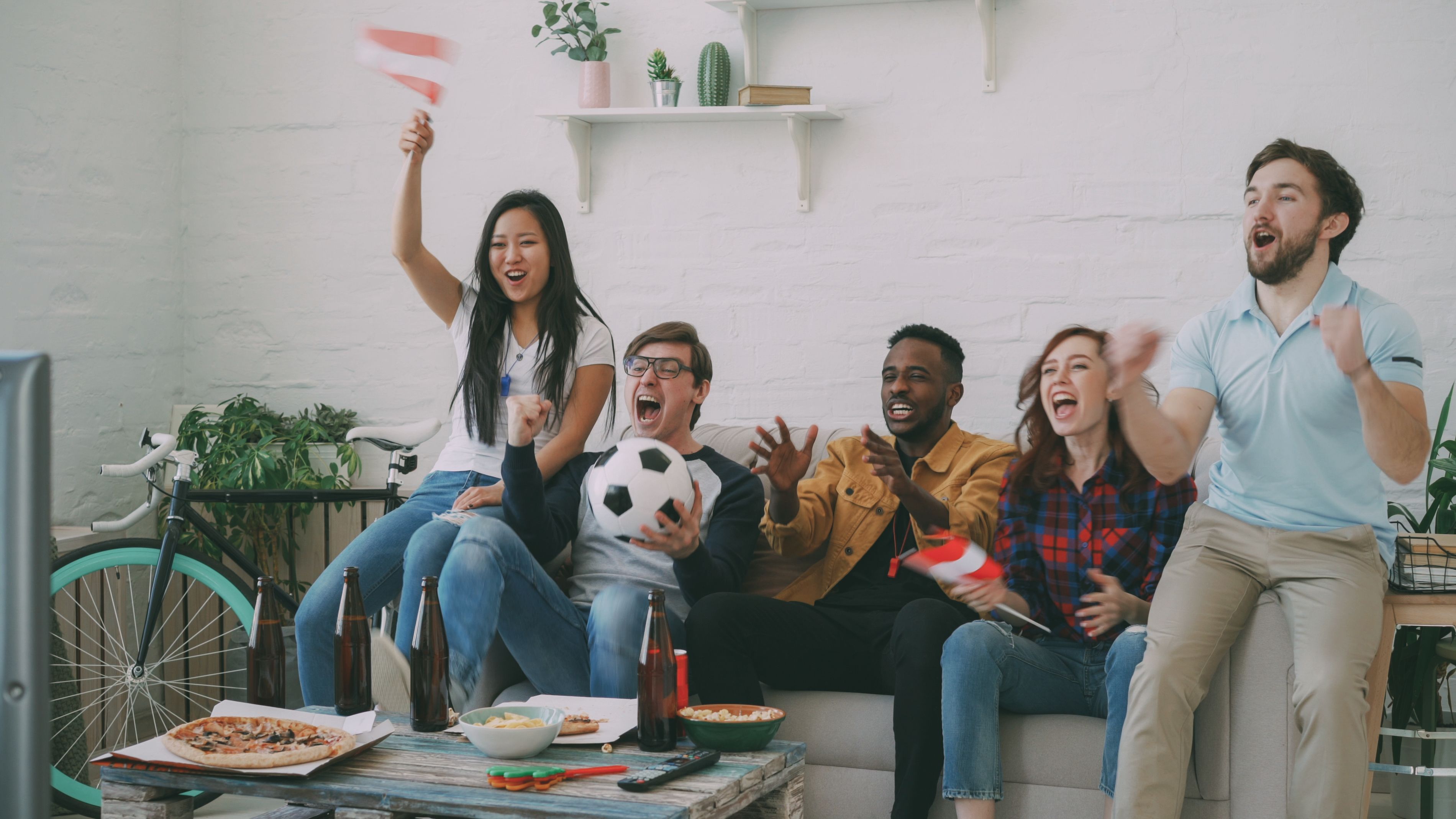 Group of friends cheering excitedly while watching a live sports game on TV at home