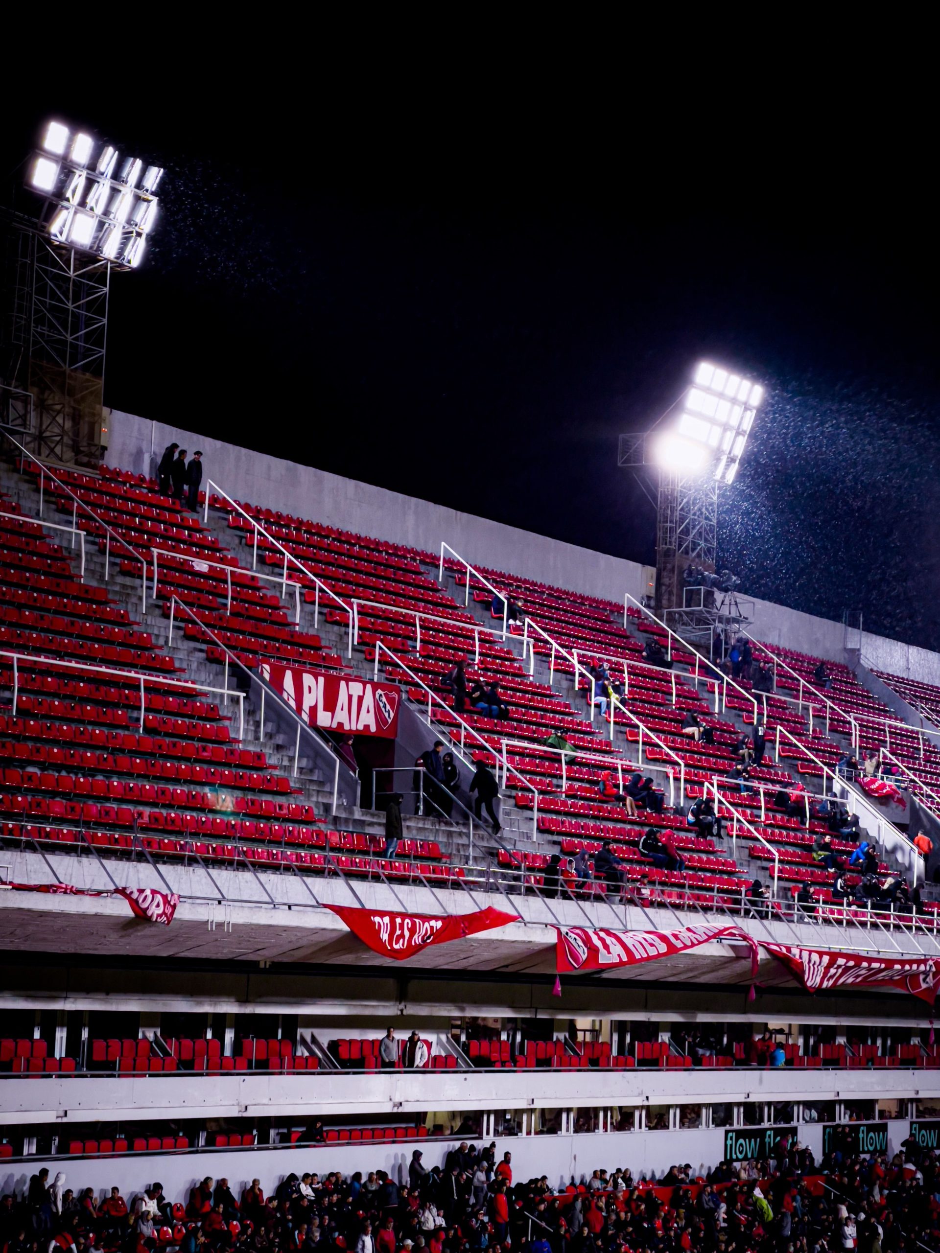 Illuminated football stadium at night with red bleachers and bright spotlights