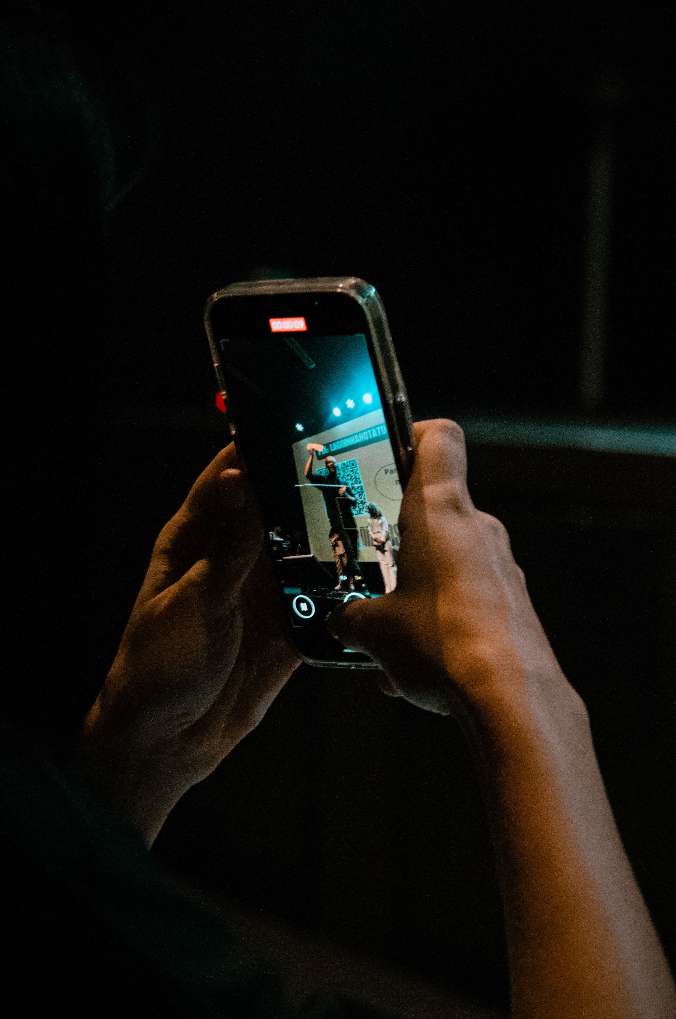 Fan filming a live sports event on a smartphone from the stands in a dimly lit arena